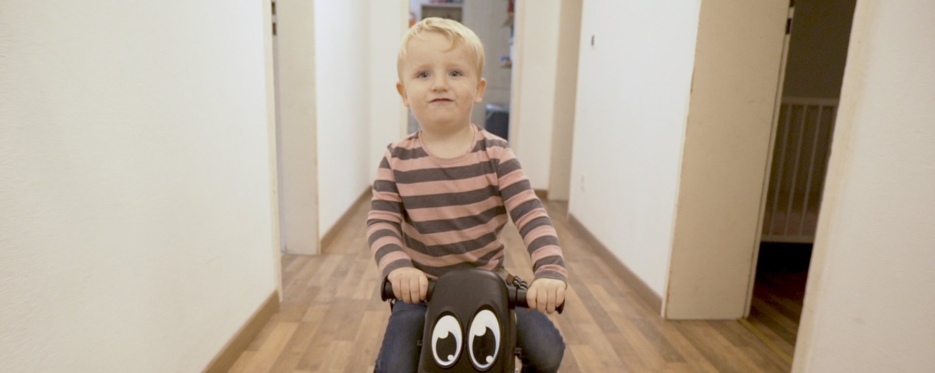 Kleiner Junge fährt fröhlich auf einem Laufrad mit Augen durch den Flur vom Mutter-Kind-Haus in Rosenheim