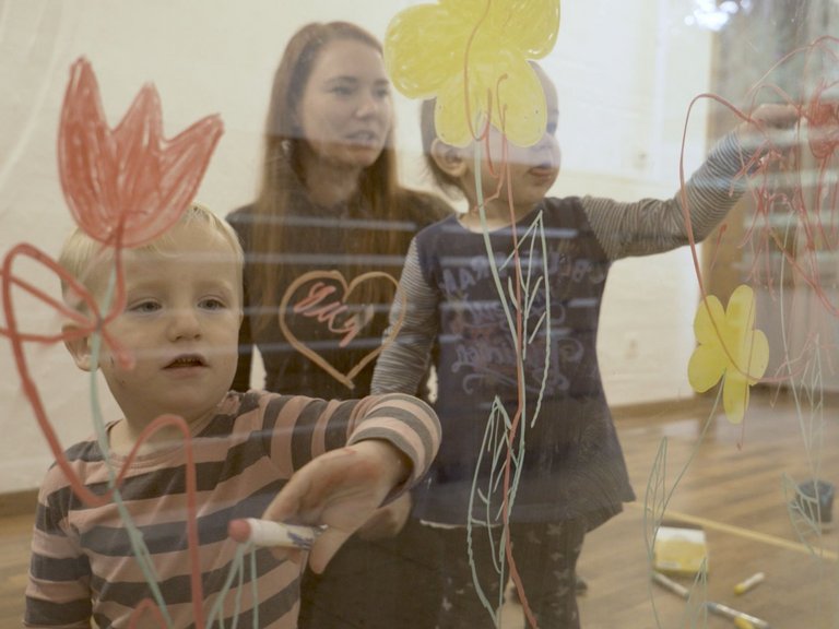 Kinder bemalen mit bunten Malfarben eine Glaswand im Mutter-Kind-Haus