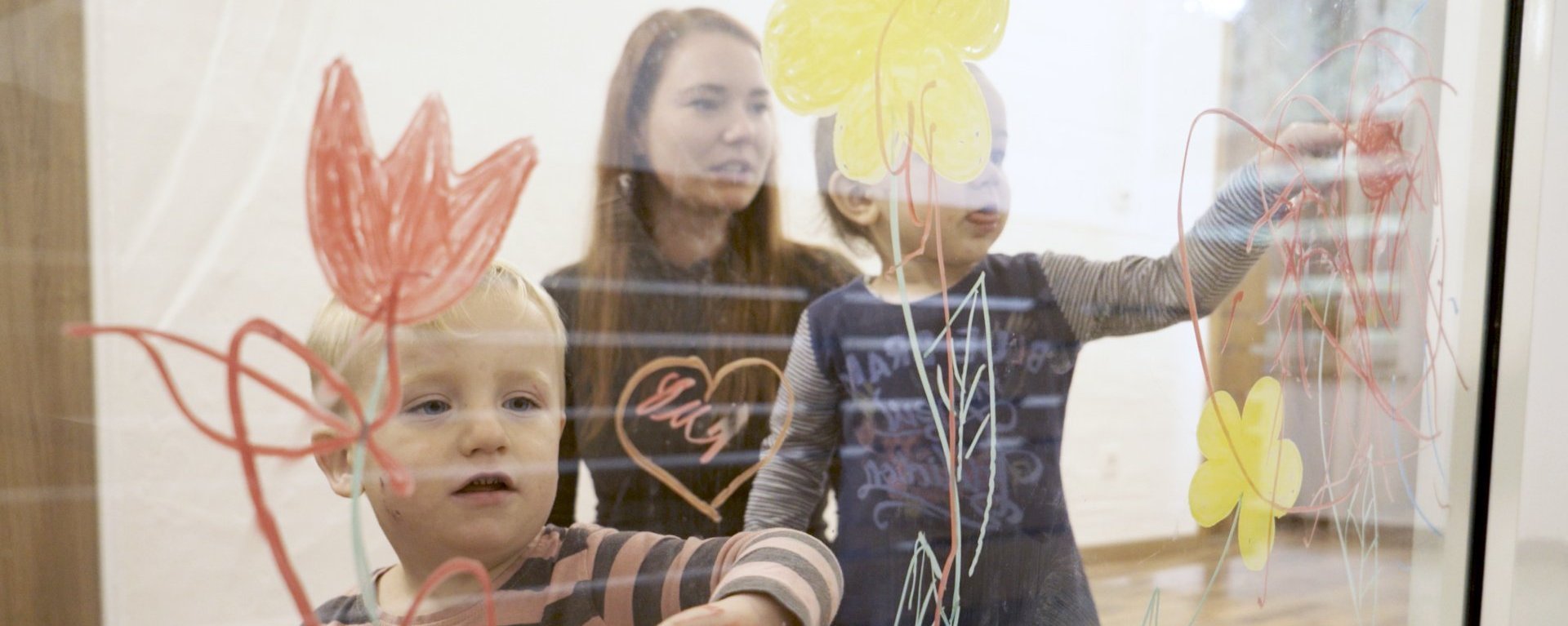 Kinder bemalen mit bunten Malfarben eine Glaswand im Mutter-Kind-Haus